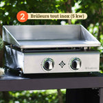 Vivaplancha stainless steel plancha with two all-stainless steel 5 kW burners, placed on an outdoor trolley, surrounded by vegetation in the background.