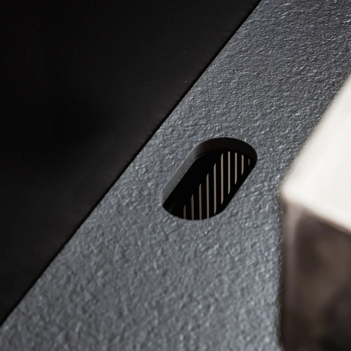 Detail of the cable grommet integrated into the black ceramic worktop Pilotis.\n::visuel:noir