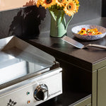 Olive green Pilotis outdoor kitchen with a Vivaplancha griddle and a black ceramic worktop.
::visuel:noir