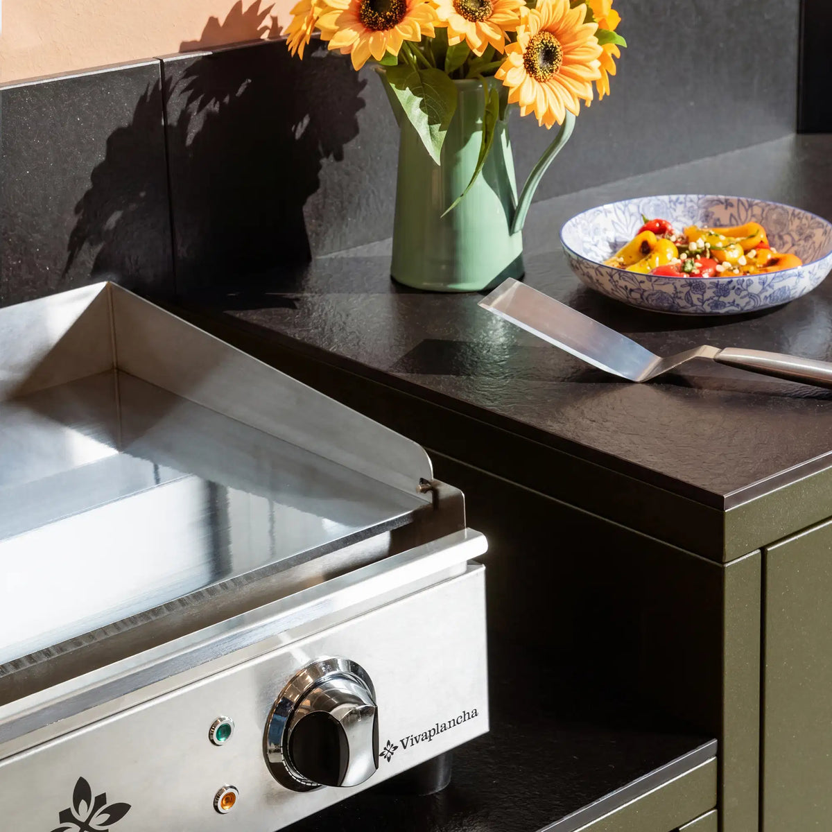 Olive green Pilotis outdoor kitchen with a Vivaplancha griddle and a black ceramic worktop.
::visuel:noir