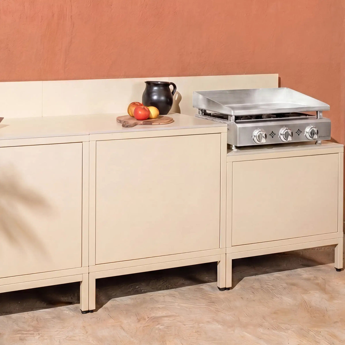 Cream-white Pilotis outdoor kitchen with integrated Vivaplancha griddle.\n::visuel:creme