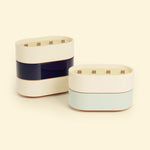 Bougies Totem L Beige ivoire – Citronnelle & Citron, Bleu marine – Citronnelle & Sel de mer et Vert d’eau – Citronnelle & Eucalyptus, deux grandes bougies ovales à triple mèche en bois, posées sur un fond beige clair.