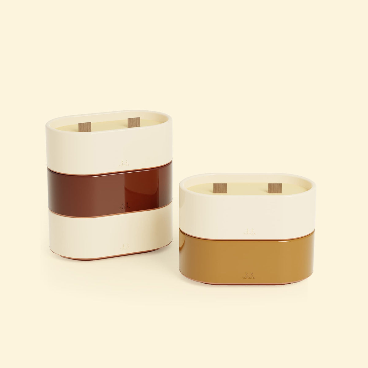 Bougies Totem S Beige ivoire – Citronnelle & Citron, Rouge oxyde – Citronnelle & Géranium et Brun terre de sienne – Citronnelle & Fleur d’oranger, deux bougies ovales à double mèche en bois, posées sur un fond beige clair. 
