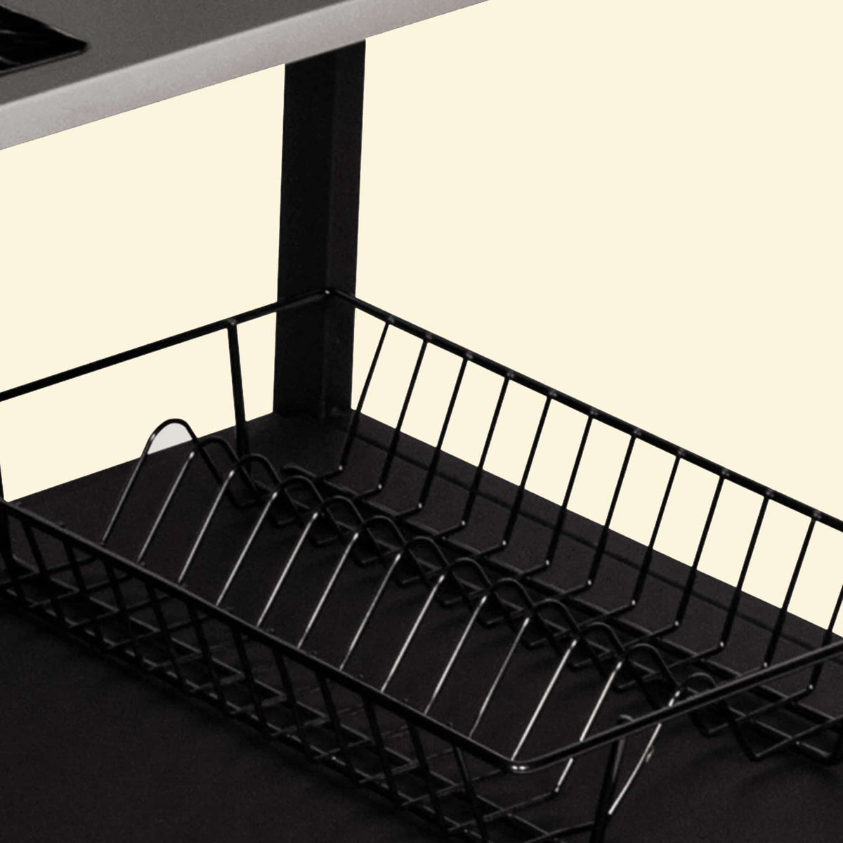 Panier de rangement en métal noir installé sur l’étagère inférieure d’un module de cuisine extérieure, présenté en gros plan sur fond clair.