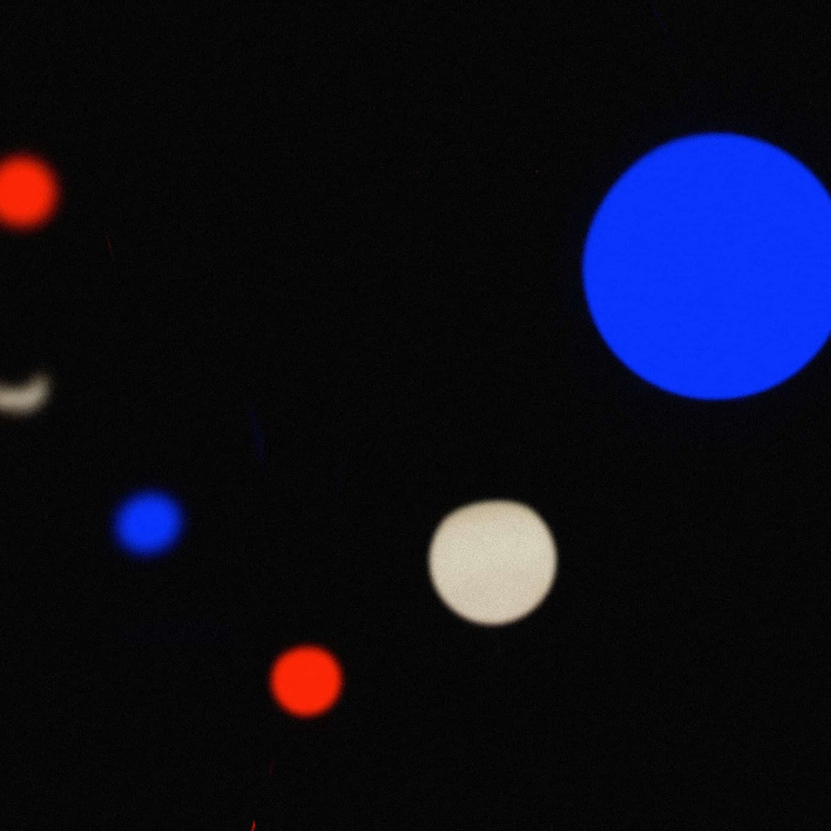 Guirlande lumineuse tricolore floue en situation nocturne, avec des points lumineux bleu, blanc et rouge ressortant sur un fond sombre pour une ambiance festive.