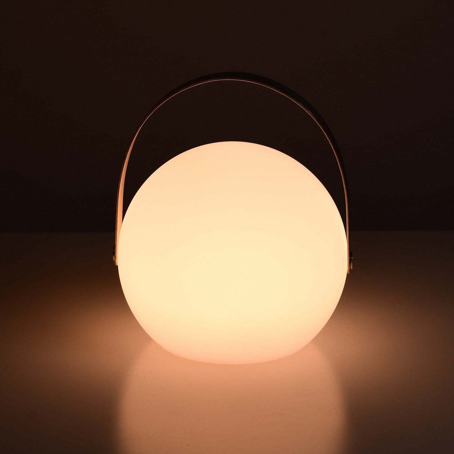 Lampe ronde solaire allumée, diffusant une lumière chaude et douce dans une ambiance tamisée, avec anse métallique arquée.