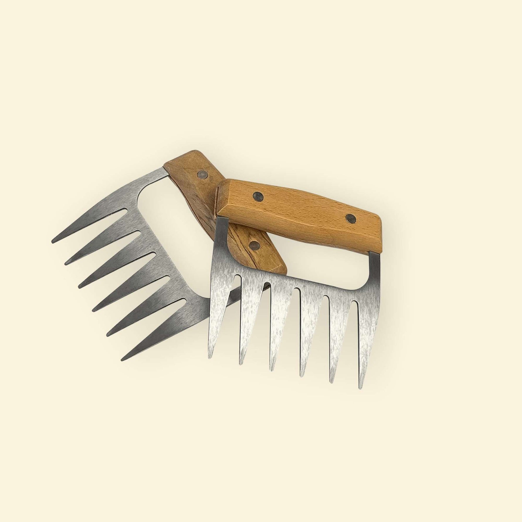 Paire de griffes à viande en inox avec poignées en bois, disposées en croix sur fond clair.