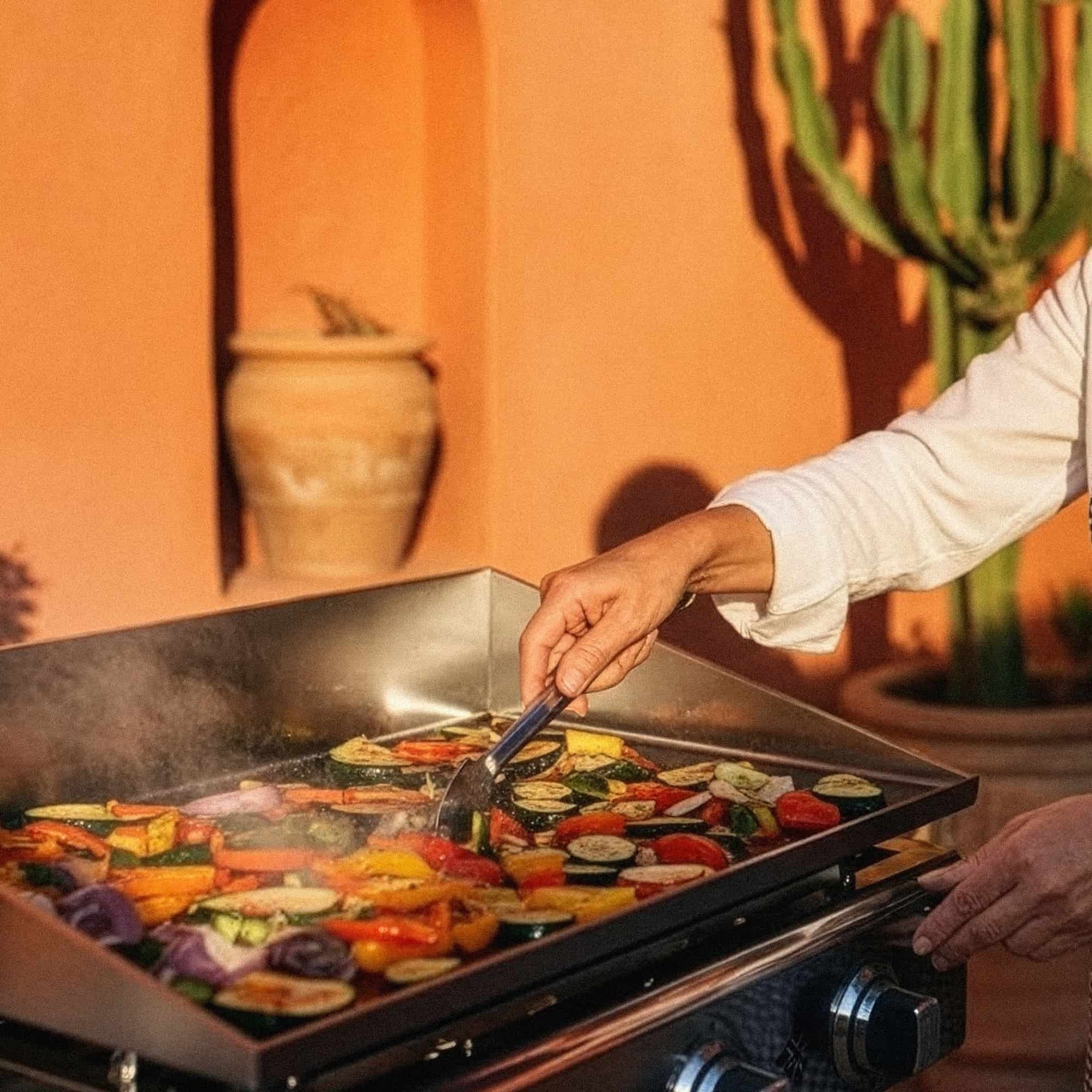 Chef cooking vegetables and meats on a Vivaplancha stainless steel griddle, expertly controlling high-temperature cooking