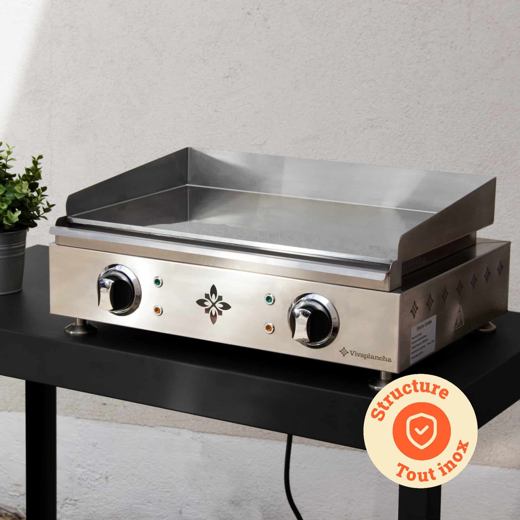 Vivaplancha plancha placed on an outdoor table, with its fully stainless steel structure highlighted and a “All stainless steel structure” badge displayed in an orange circle.